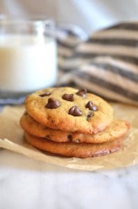 Chocolate chip cookies on parchment paper with glass of milk in the background.