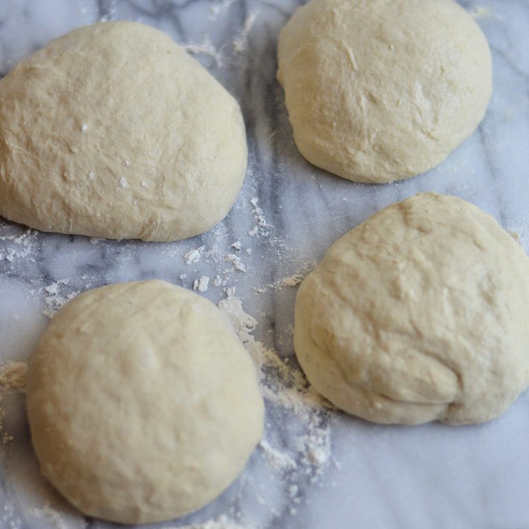 4 pizza dough balls on a marble surface.