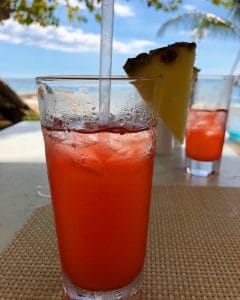 A red cocktail garnished with a pineapple wedge.