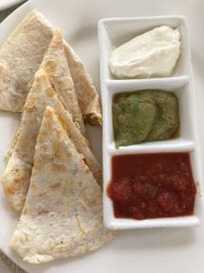 A quesadilla on a plate with salsa, guacamole and sour cream.