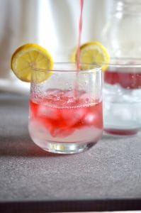Passion Tea being added to lemonade in a short glass with ice and lemon slice.