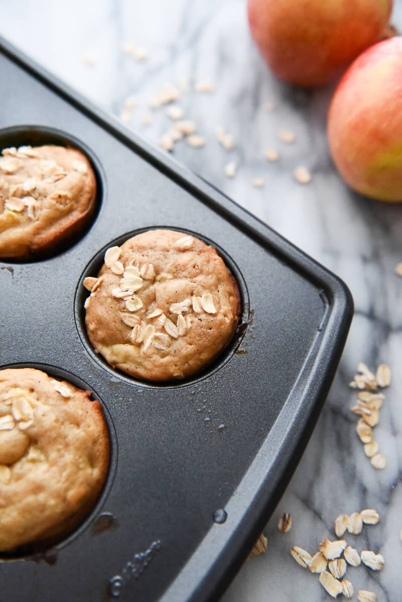A close up photo of an Apple Cinnamon Oatmeal Muffin in its baking pan with old fashioned oats sprinkled on top.