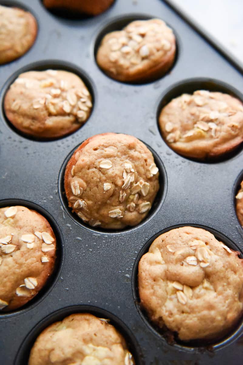 A close up shot of Apple Cinnamon Oatmeal Muffins in its baking pan with old fashioned oats sprinkled on top of each muffin.